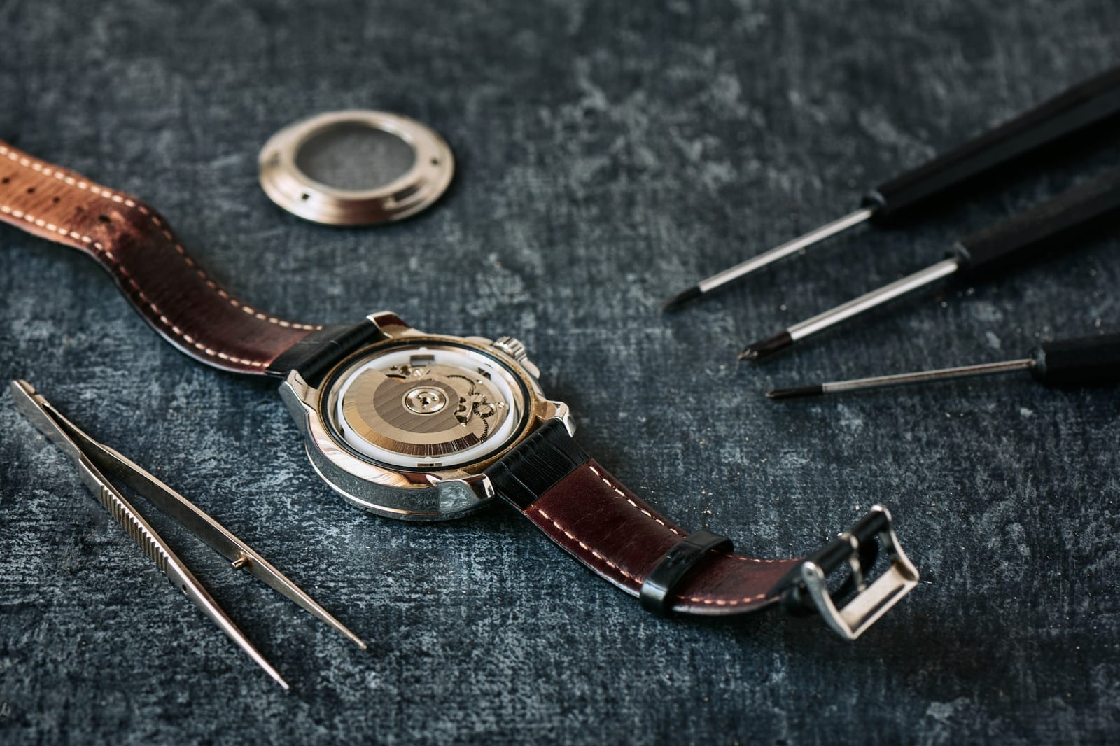 Tavolo di lavoro con tweezer e componenti di un bracciale metallico in fase di riparazione